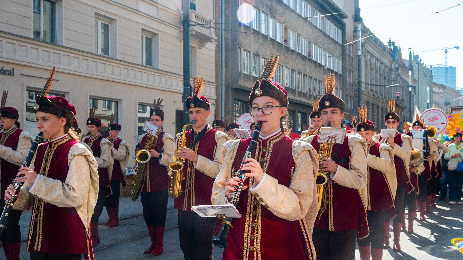 Na zdjęciu orkiestra w kolorowych strojach, widać ludzi grających na instrumentach dętych