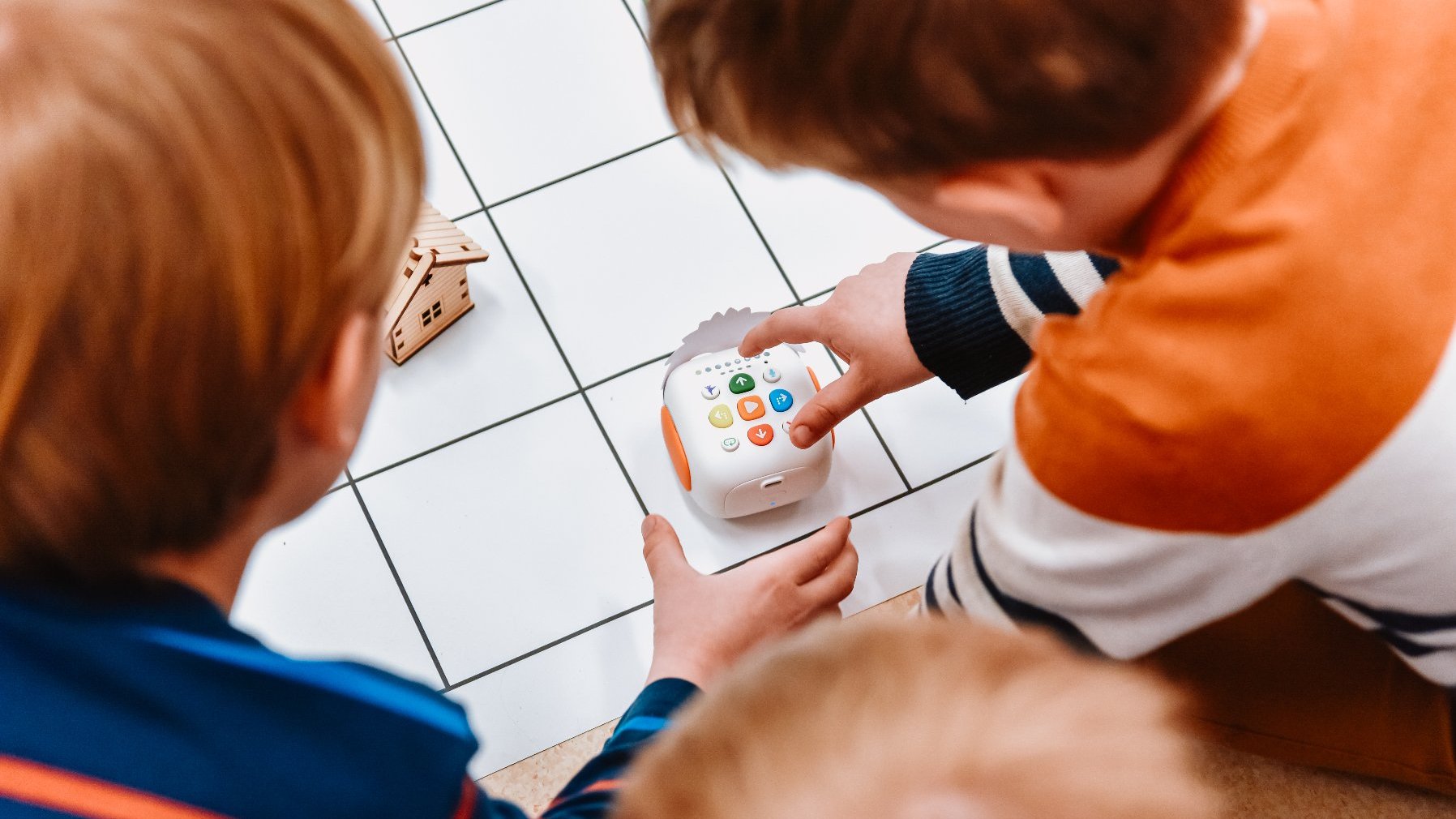 Zdjęcie przedstawia dzieci siedzące na macie i bawiące się robotem.