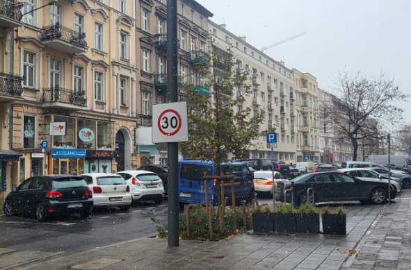 Widok na ulicę Ratajczaka. Po prawej stronie znajduje się chodnik. Po obu stronach ulicy ciąg zaparkowanych samochodów. W tle kamienice. - grafika artykułu