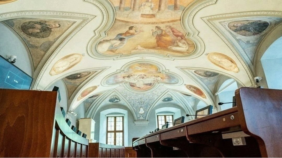 Sala sesyjna Rady Miasta Poznania, pusta, widoczne stanowiska radnych i zdobiące sufit zabytkowe freski - grafika artykułu