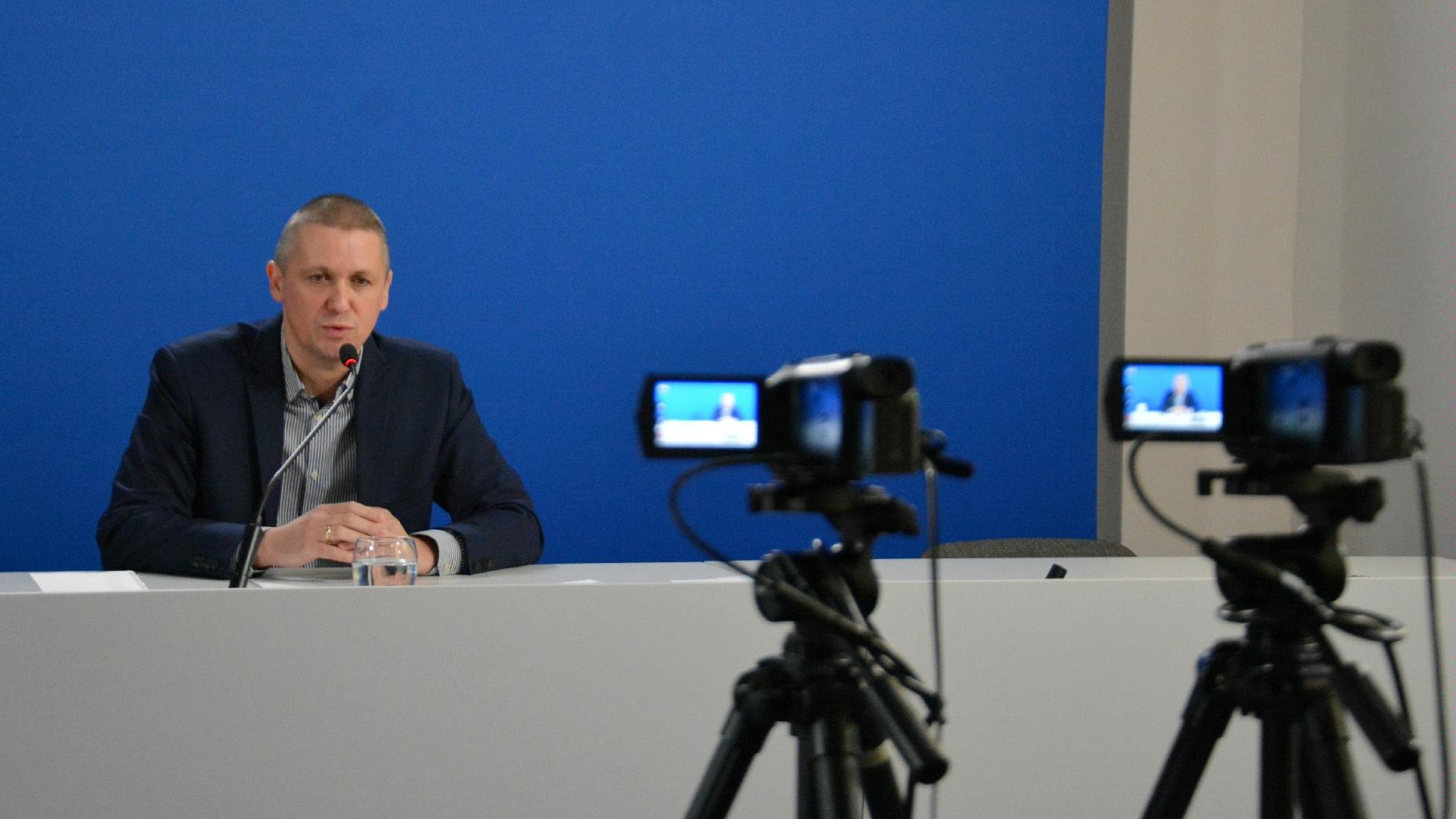 Zdjęcie przedstawia Patryka Pawełczaka, dyrektora Gabinetu Prezydenta UMP. Dyrektor siedzi za biurkiem, na pierwszym planie widać kamery. - grafika artykułu