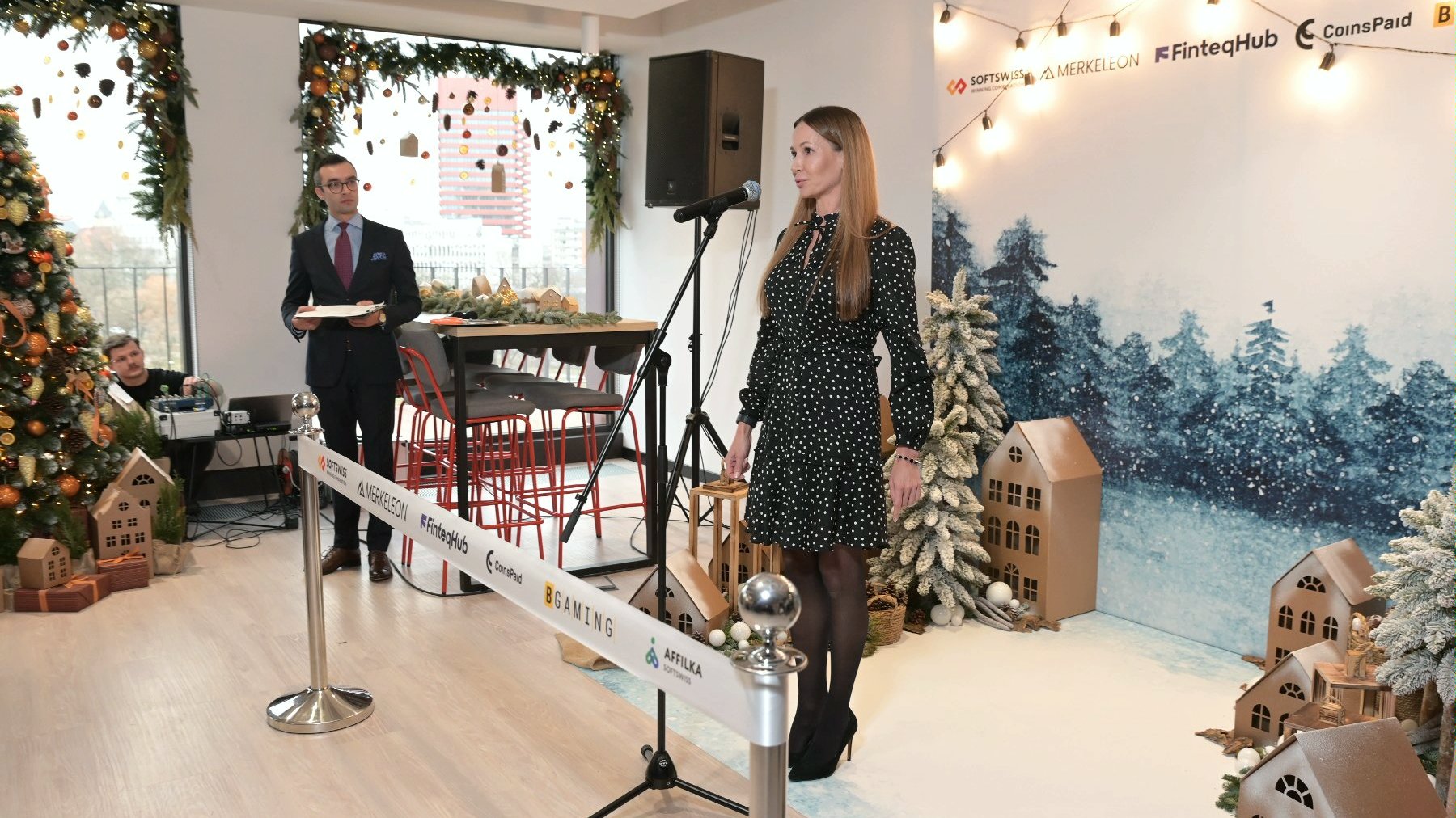 The photo shows Katja Lozina, director of the Investor Relations Department, speaking. In the background is a festive wall with company logos, including SOFTSWISS.