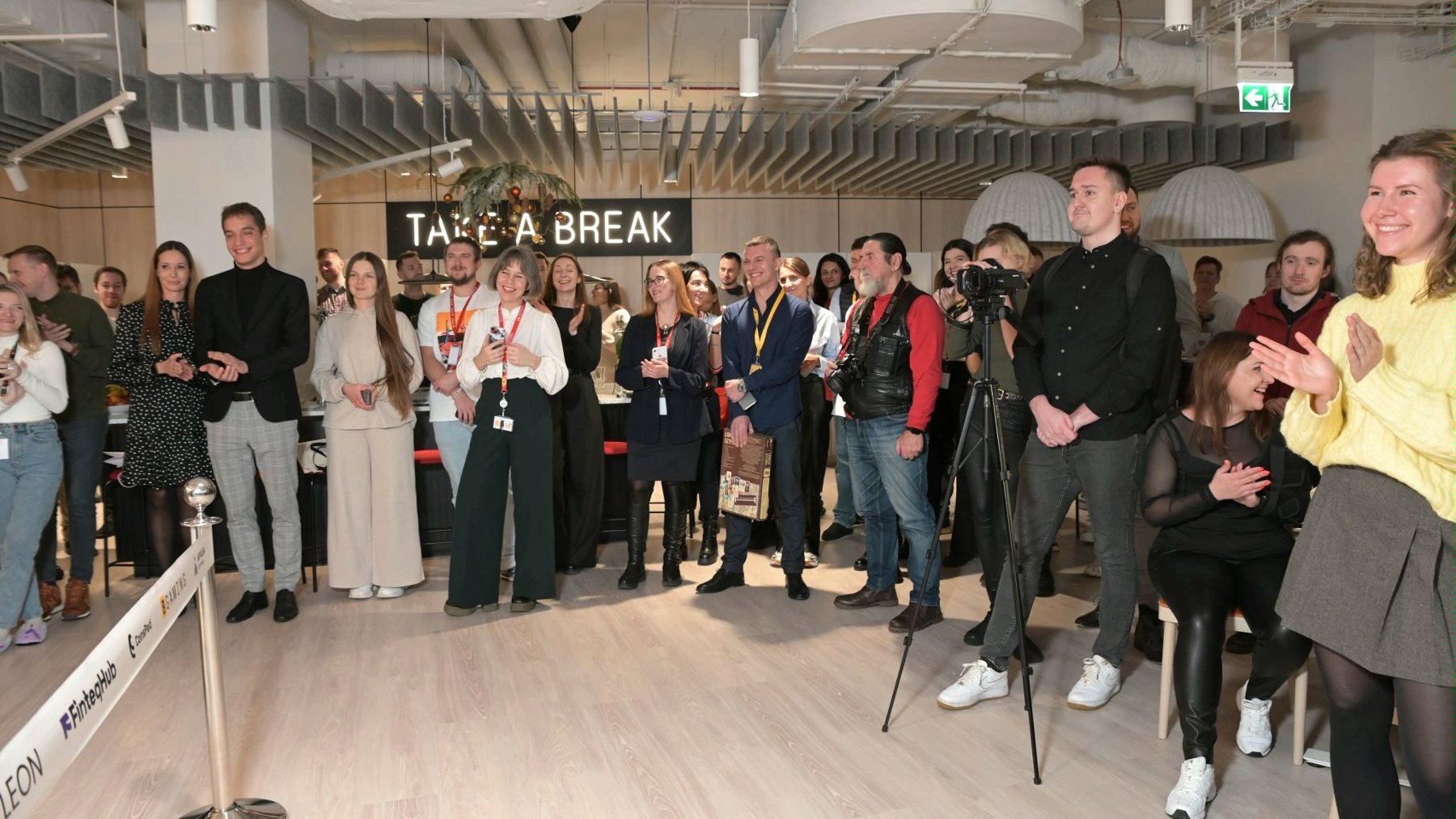 The photo shows a group of people attending the opening of the SOFTSWISS office. The individuals are smiling, clapping. They are facing an unseen stage.