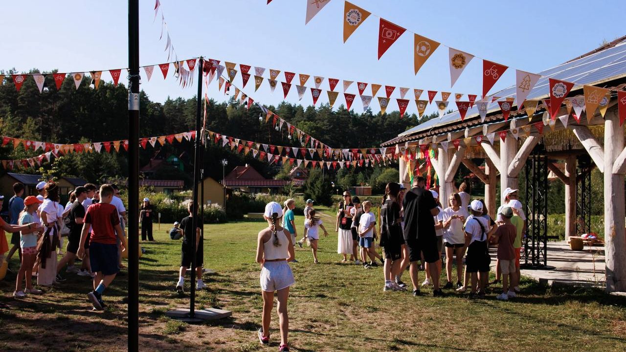 Photo from the children's camp, wooden shelter on the right, trees in the back, crowd of children in front