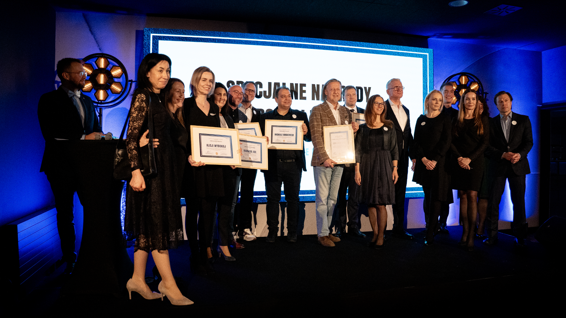 A group of people honoured by the Investor Relations Department with awards. They stand on stage, all dressed in evening wear. - grafika artykułu