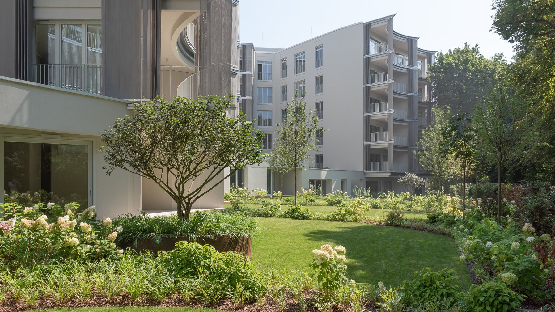 Gardens in front of Perfumiarnia. Lush greenery grows around the modern blocks of flats.