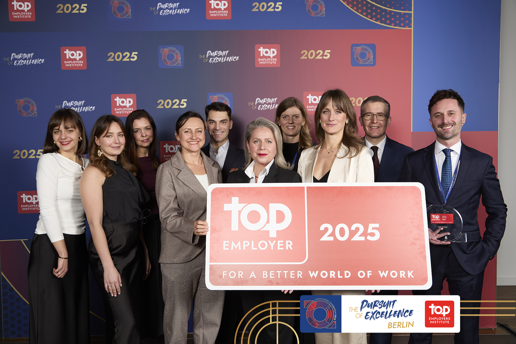 A group of people dressed in elegant outfits. They pose with the Top Employer 2025 award statuette. - grafika artykułu