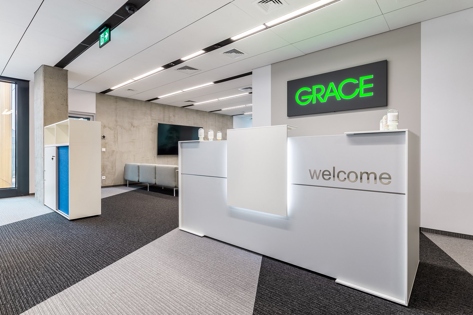 Zdjęcie przedstawia białą ścianę, widnieje na niej logo firmy Grace. Przed nim znajduje się biała recepcja z napisem "Welcome". - grafika artykułu