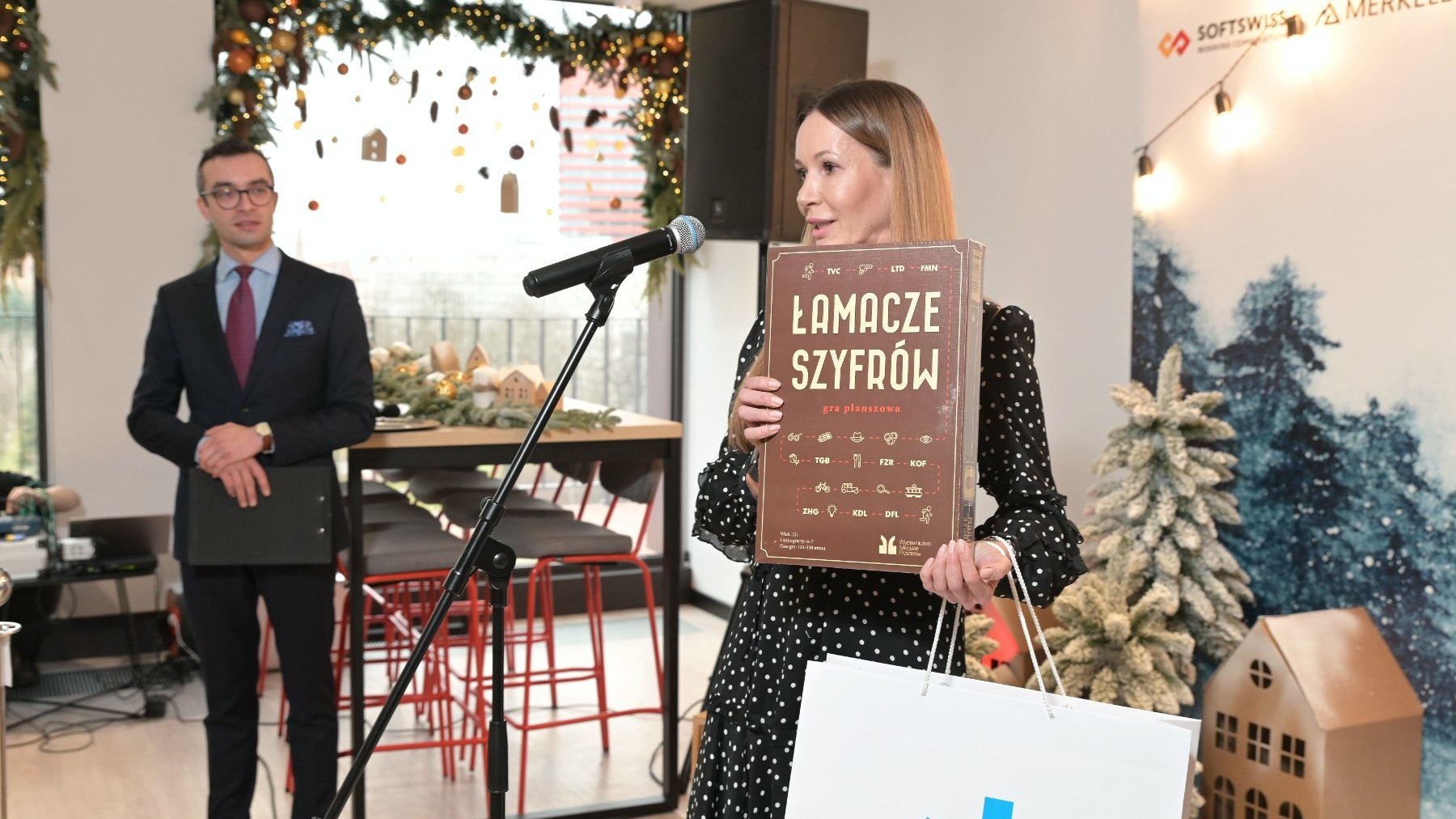 Zdjęcie przedstawia dyrektor Biura Obsługi Inwestorów Katję Lożinę. Prezentuje grę planszową "Łamacze szyfrów".