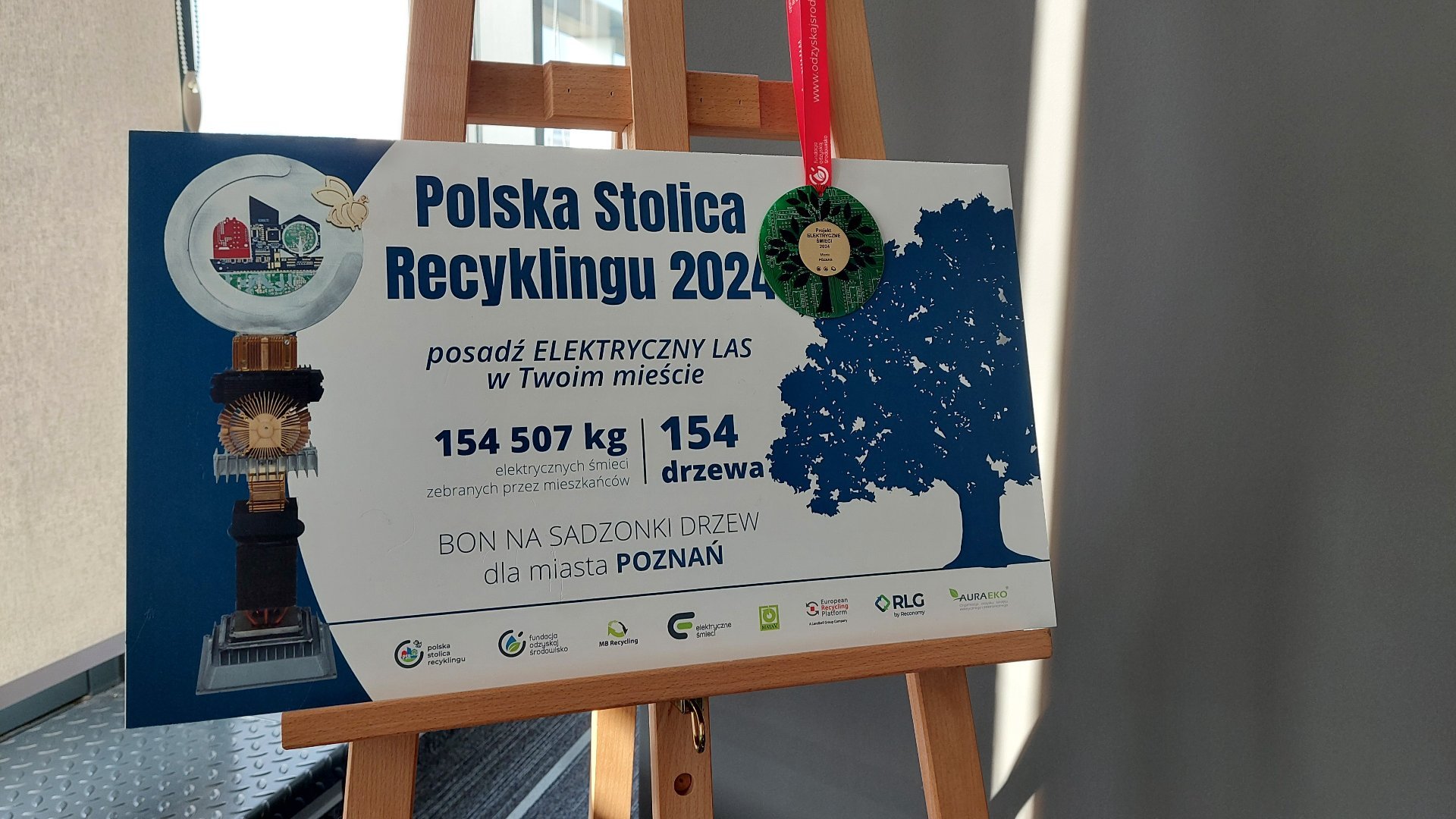 Zdjęcie przedstawia tablicę na stelażu z informacją o wynikach, jakie Poznań uzyskał w konkursie.