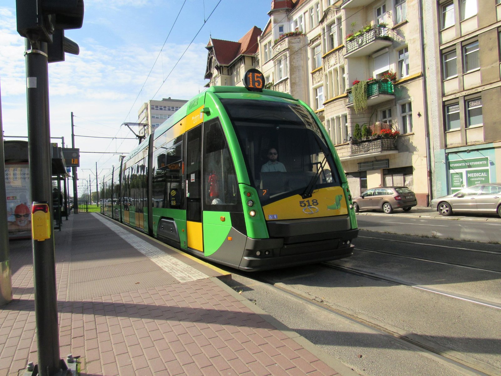 Zielony tramwaj nr 15 na przystanku, iwidziany od przodu. W tle kamienice miejskie. - grafika artykułu