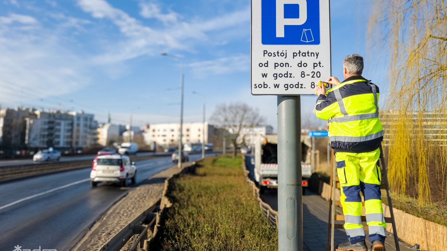 Zdjęcie osoby stojącej na drabince zmieniającej godzinę na tablicy z literą P przymocowaną do słupa przy drodze