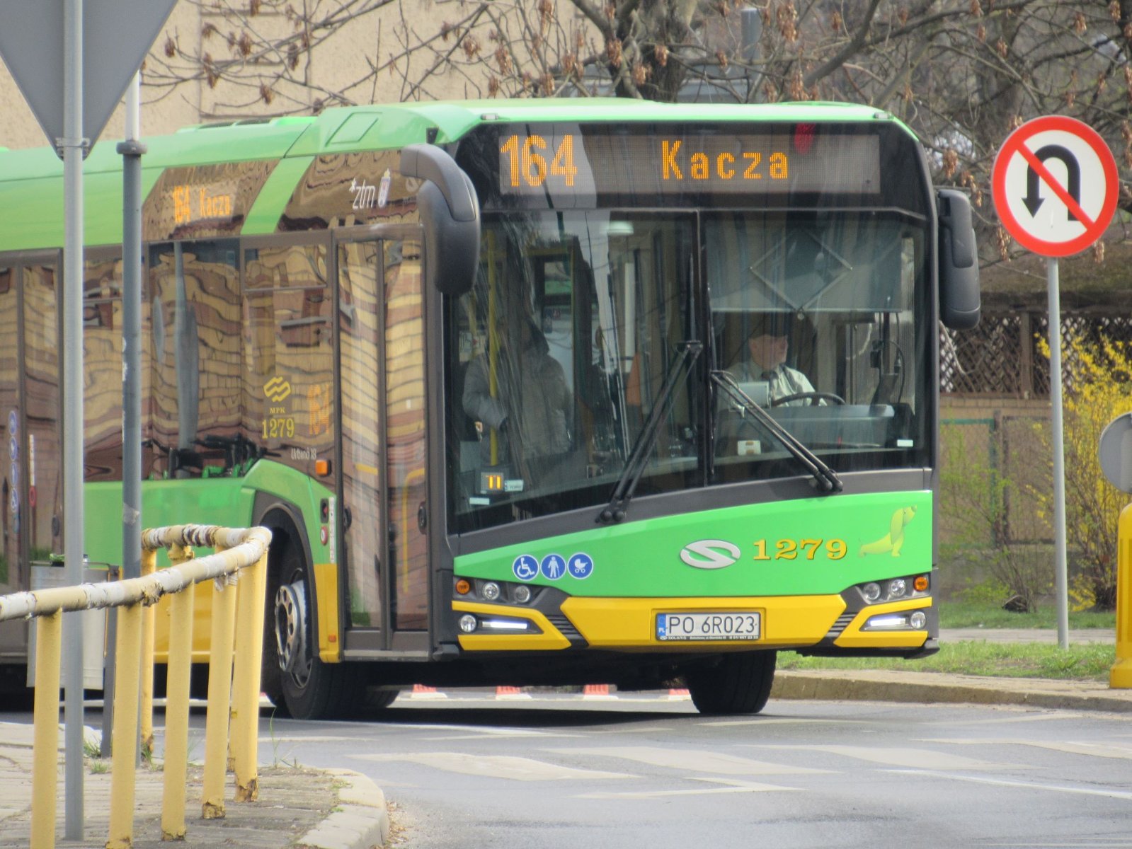 Zielony autobus linii nr 164 jedzie na zakręcie w stronę petli Kacza. Wzdłuż jezdni żółta metalowa barierka i znaki drogowe. - grafika artykułu