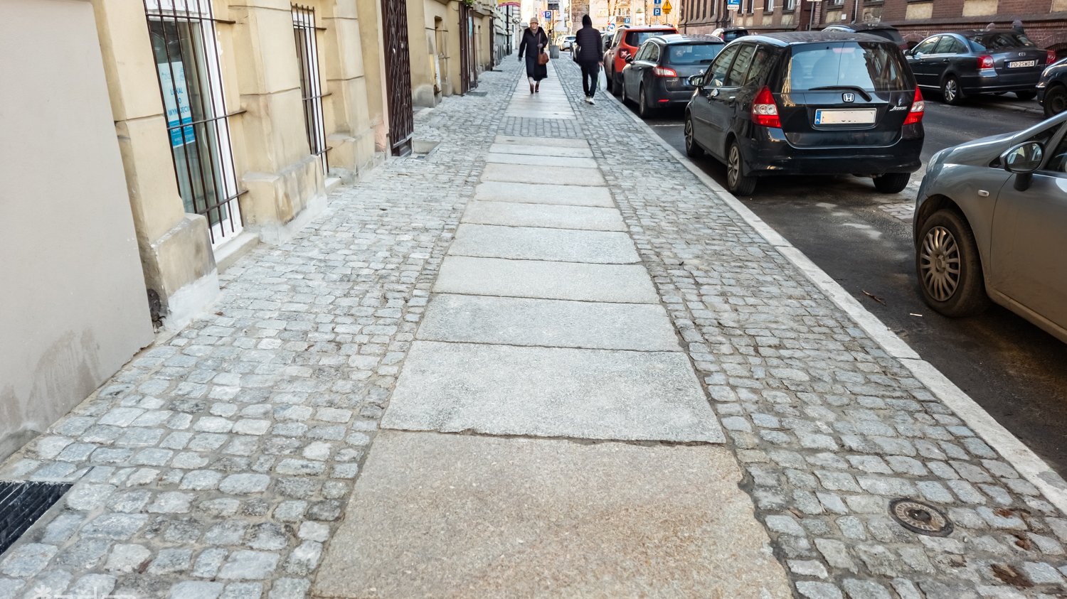 Chodnik przy ul. Łąkowej, ludzie idą po nowych płytkach wzdłuż ciągu kamienic, po prawej miejsca postojowe na jezdni