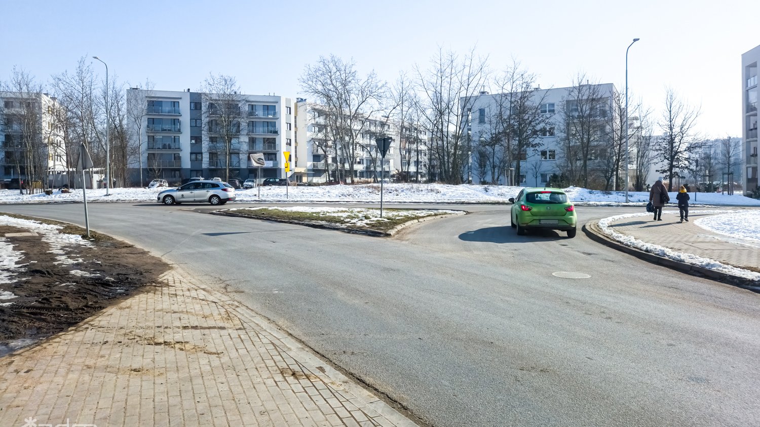 Zdjęcie skrzyżowania, które zmieni się w rondo, przejeżdżają dwa dwa samochody osobowe, w tle budynki