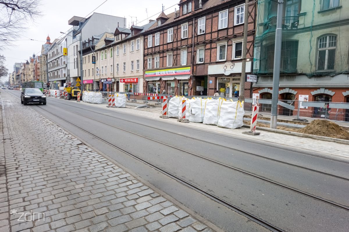 Przebudowywany odcinek ul. Dąbrowskiego, materiały budowlane i słupki ostrzagawcze na skraju jezdni - grafika artykułu