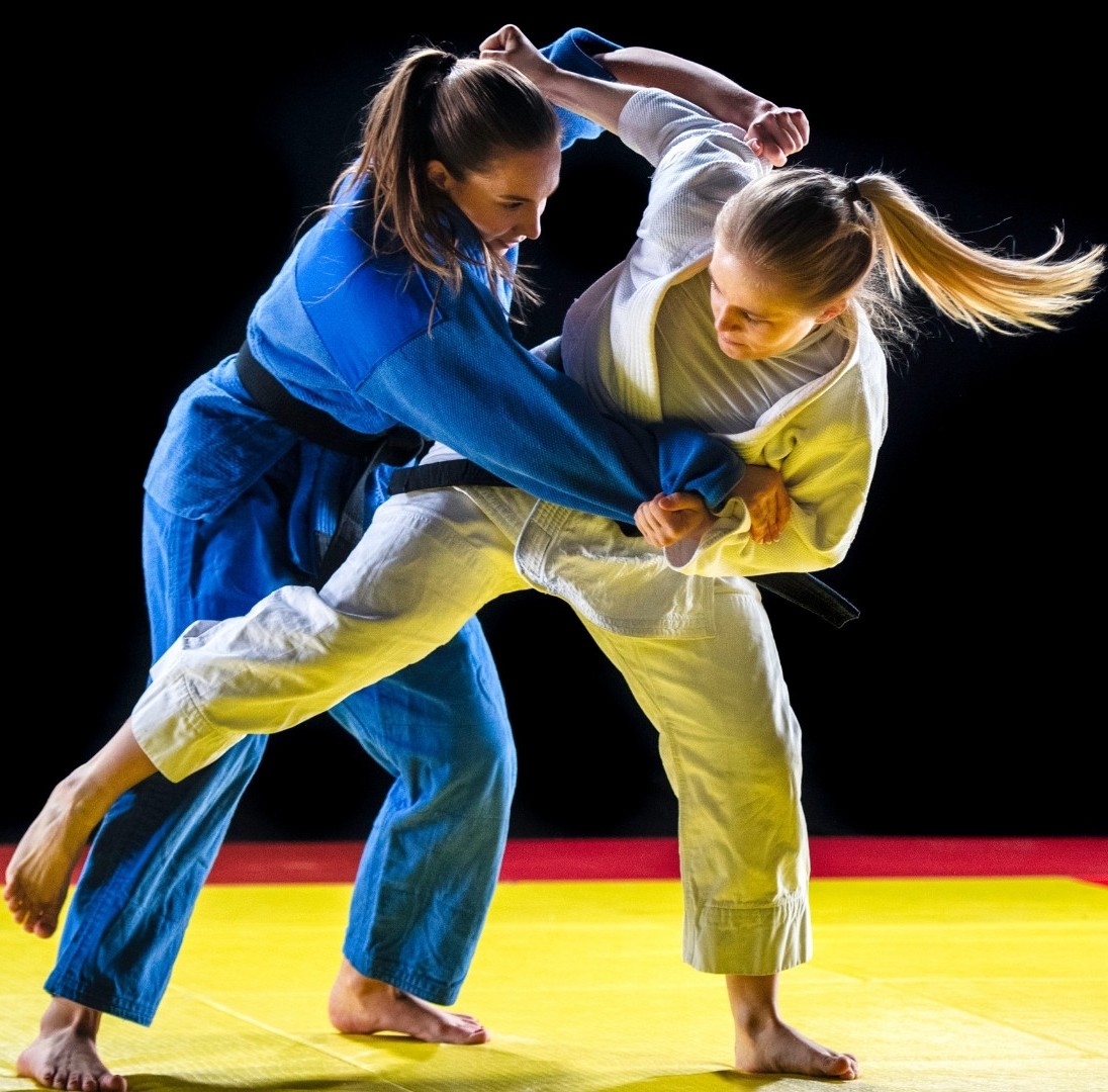 Dwie zawodniczki judo ćwiczące na macie. Jedna ubrana w białą a druga w niebieską judogę