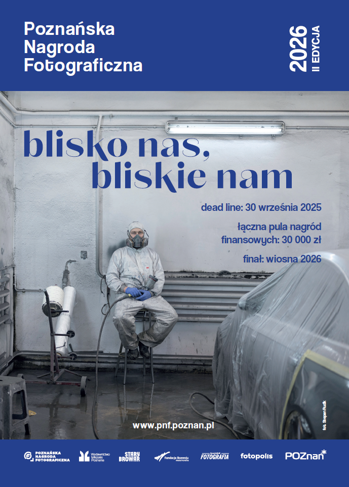 Mężczyzna ubrany w strój ochronny i maskę siedzi na stołku w warsztacie samochodowym.