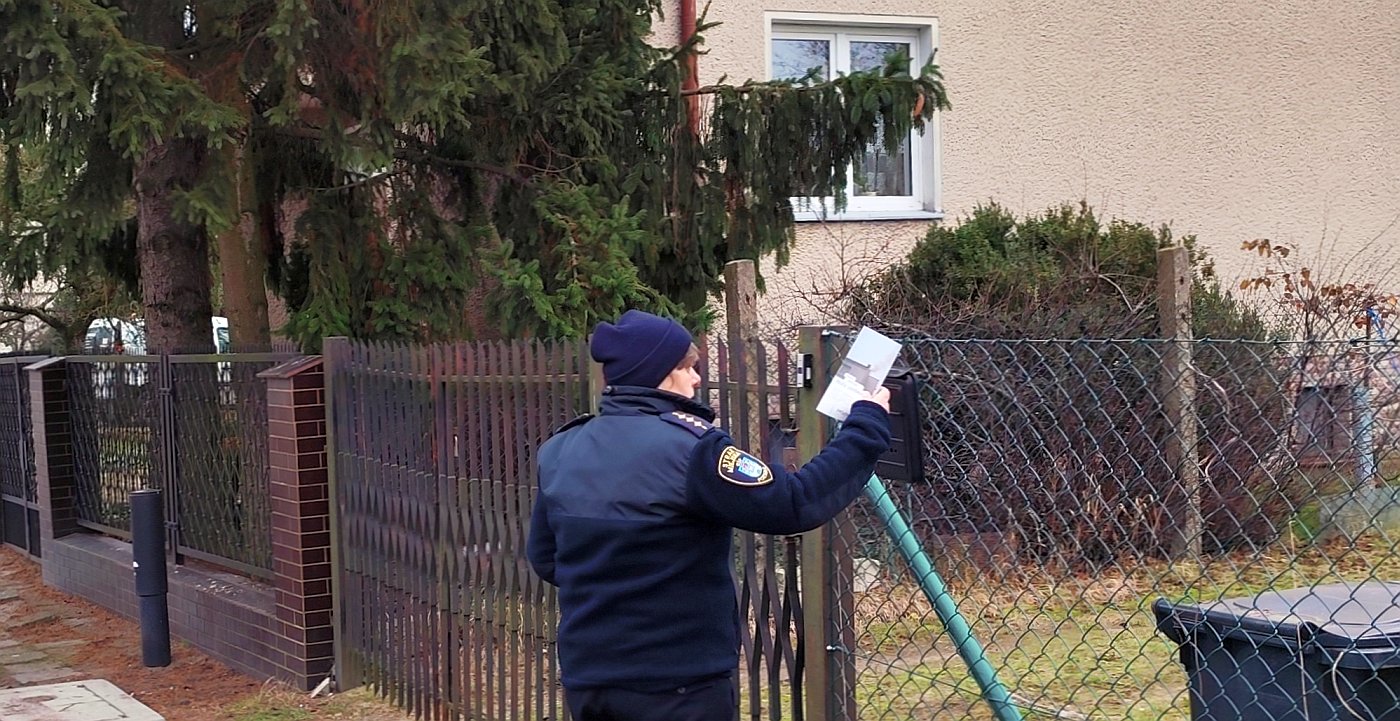 strażniczka wrzuca do skrzynki na listy ulotkę informacyjną