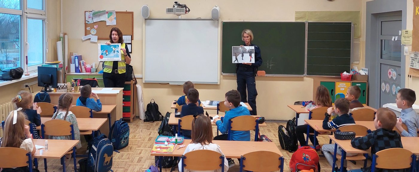 strażniczka wraz z policjantką przedstawiają sytuacje na planszach i rozmawiają z uczniami o bezpiecznym uczestniczeniu w zimowych zabawach