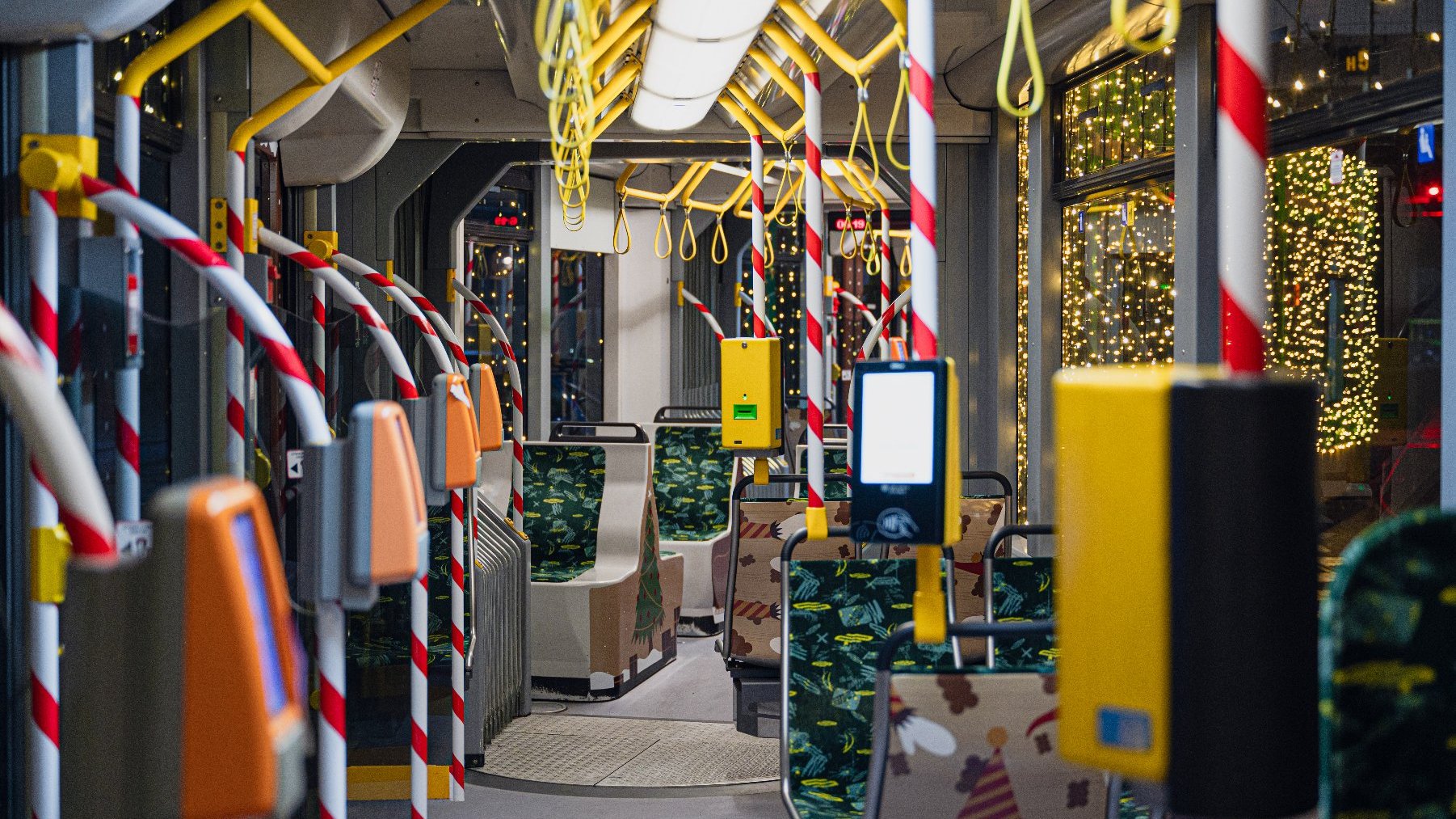 Wnętrze tramwaju. Uchwyty wyglądają jak czerwono-białe laski. Na oparciach siedzeń narysowane są rączki elfów.