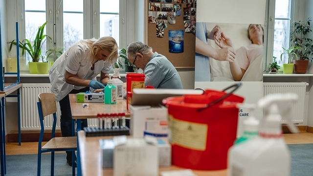 Na zdjęciu wnętrze szkoły, kobieta w białym fartuchu pochyla się nad mężczyzną