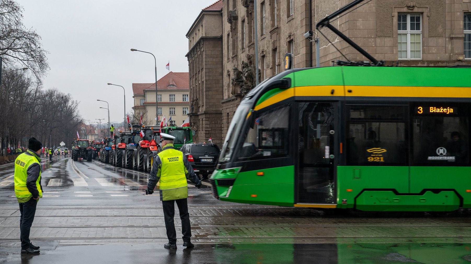 Zdjęcie przedstwia sznur ciągników na ulicy oraz tramwaj i policjantów kierujących ruchem.