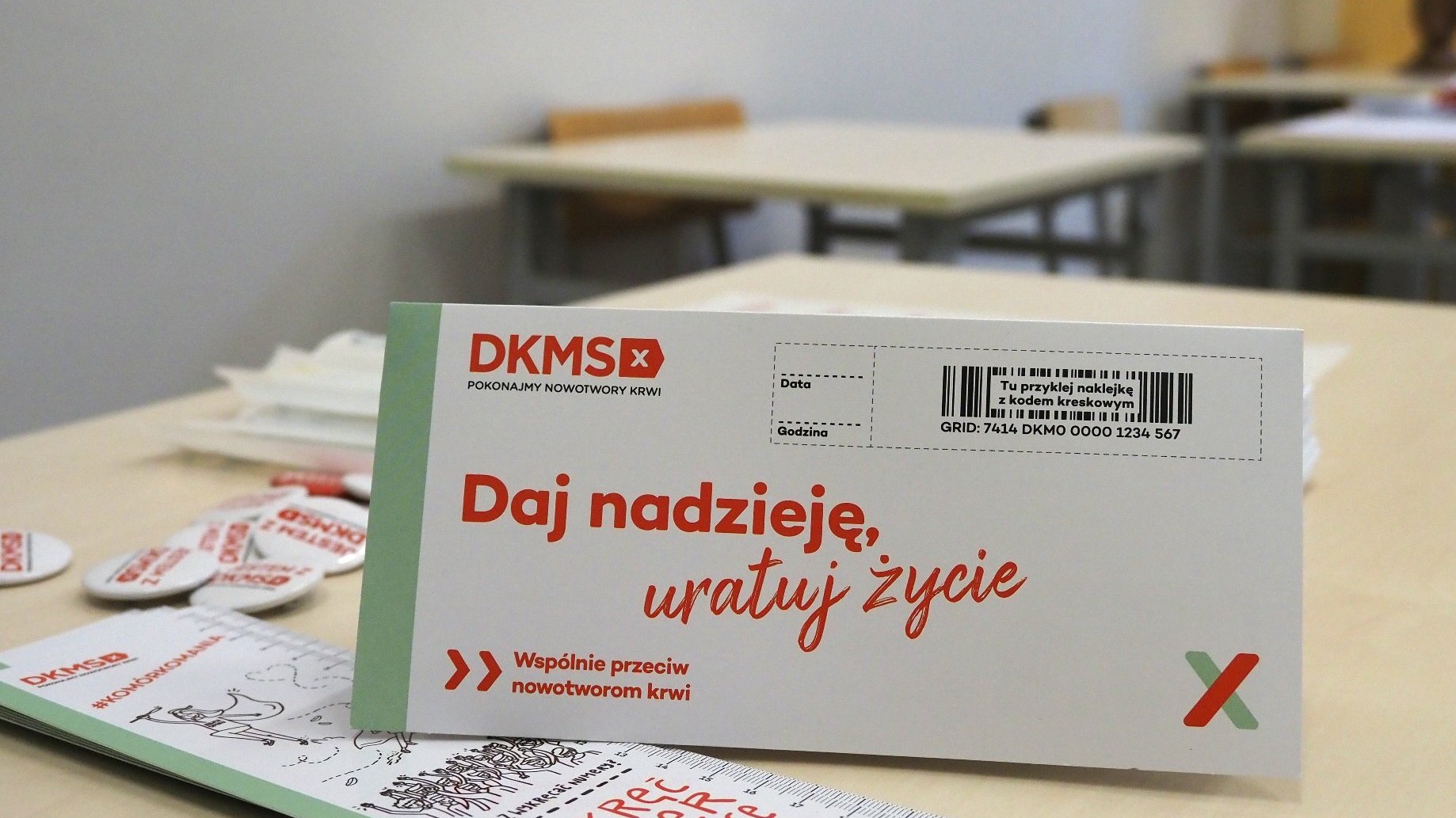 Zdjęcie przedstawia ulotki i inne gadżety Fundacji DKMS położone na ławce szkolnej.