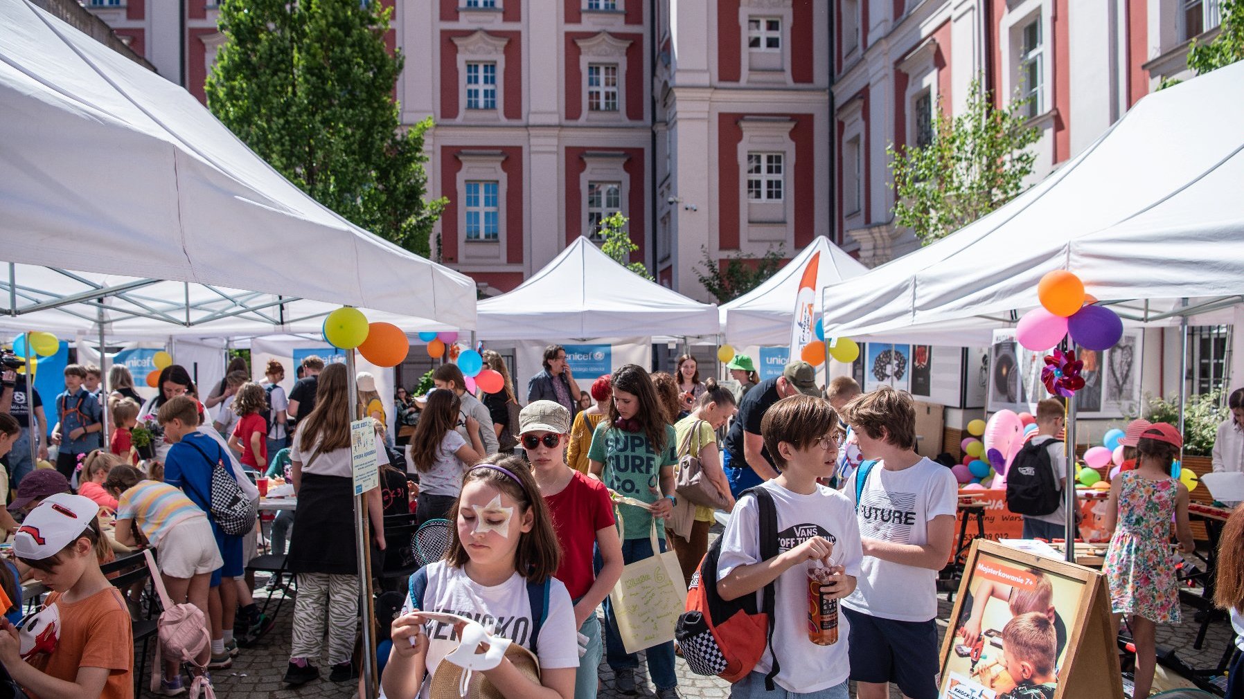 Na zdjęciu grupa dzieci na dziedzińcu urzędu, widać kolorowe balony i białe namioty