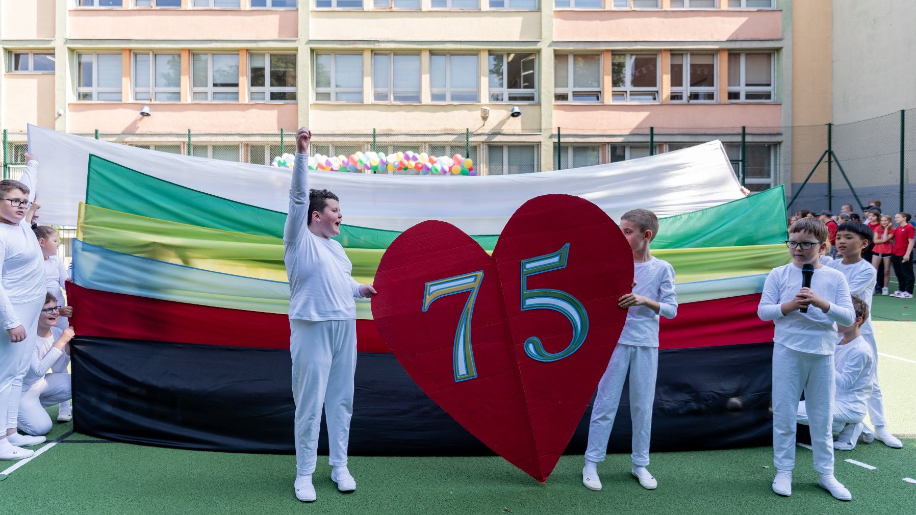 Zdjęcie przedstawia dzieci trzymające wielkie serce z numerem 75.