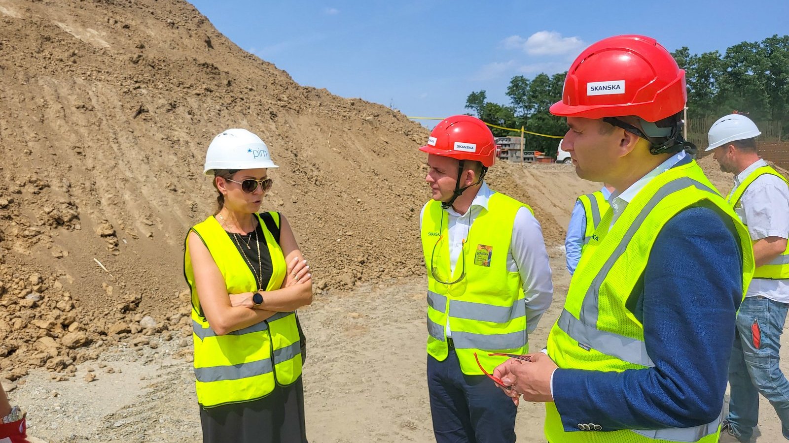 Na zdjęciu kilka osób przy hałdzie piachu na placu budowy, rozmawiają