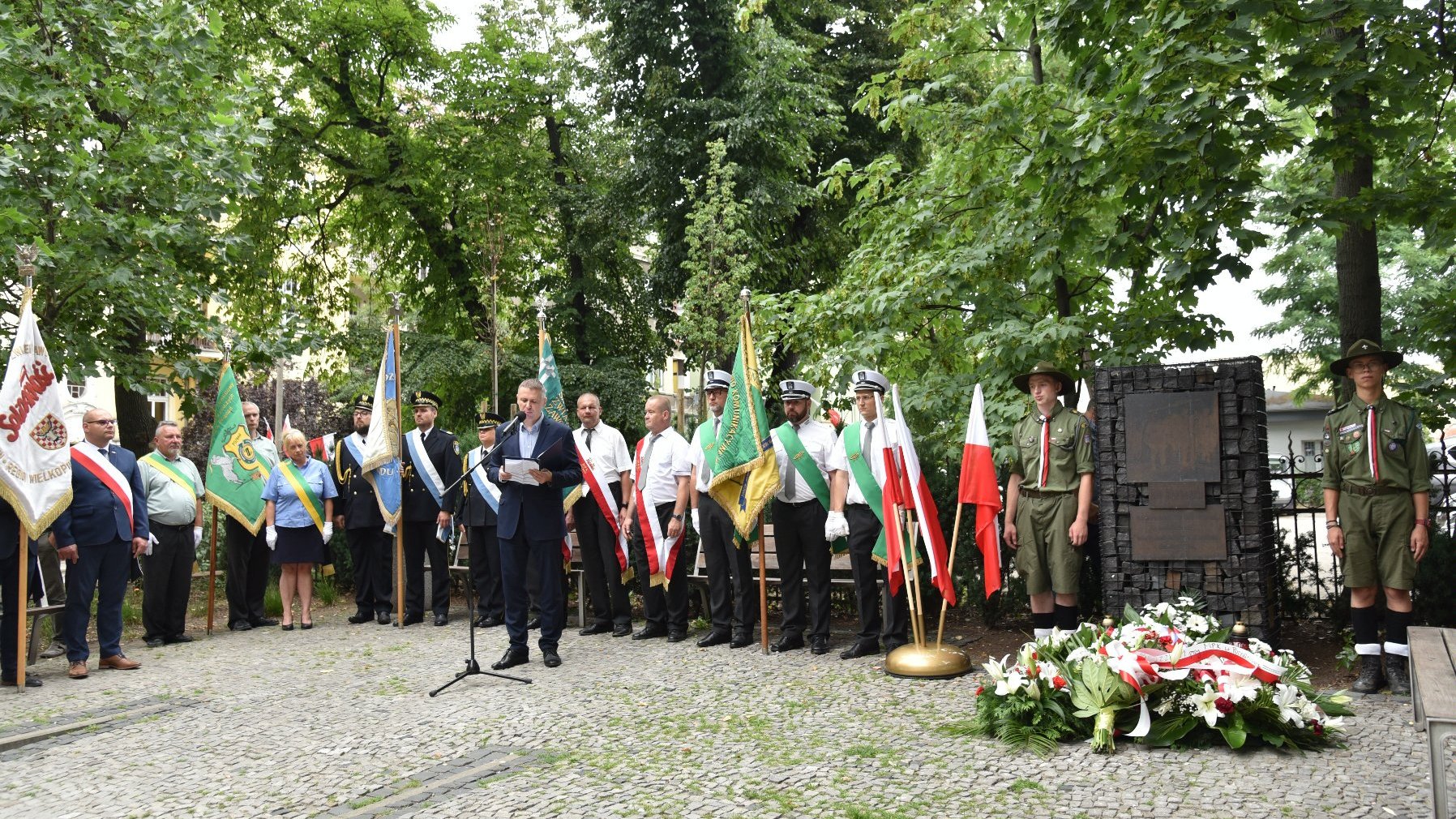 Na zdjęciu grupa ludzi wokół pomnika, widać poczty sztandarowe