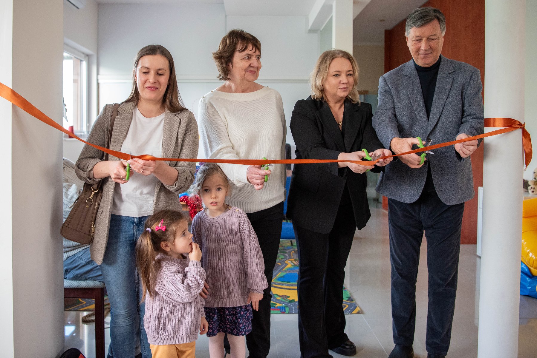 Na zdjęciu grupa ludzi przecinających wstęgi w pomieszczeniu - grafika artykułu