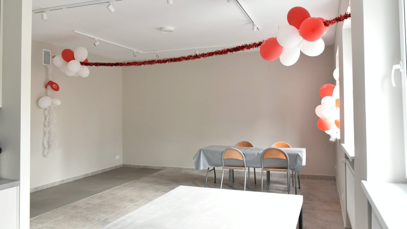 Zdjęcie przedstawia pomieszczenie świetlicy. Widać na nim balony i stoły z krzesłami.