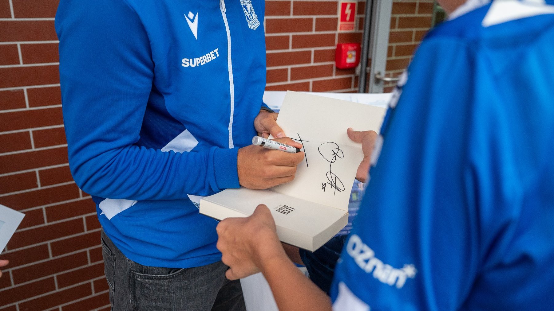 Na zdjęciu piłkarz składający autograf na książce o Lechu Poznań