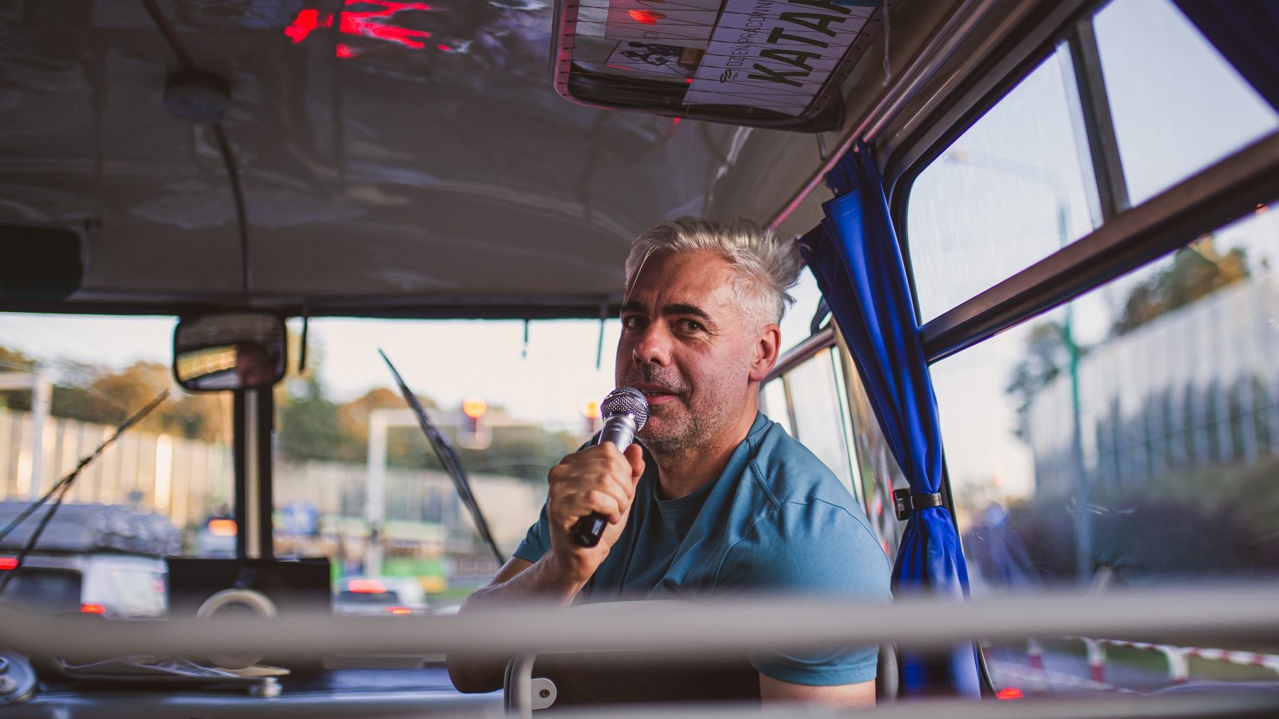 Zdjęcie przedstawia mężczynę z mikrofonem w autobusie.