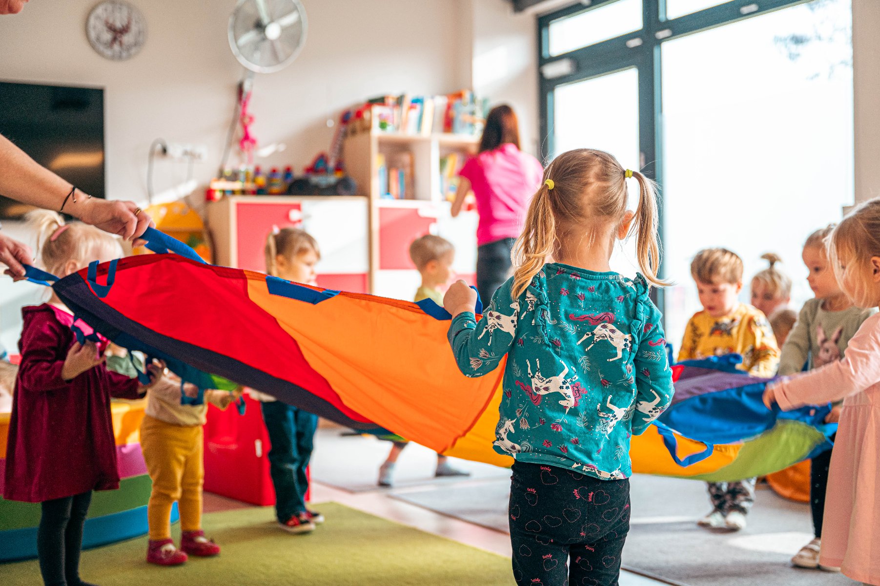 Zdjęcie przedstawia dzieci bawiące się chustą klanza w sali żłobkowej. - grafika artykułu