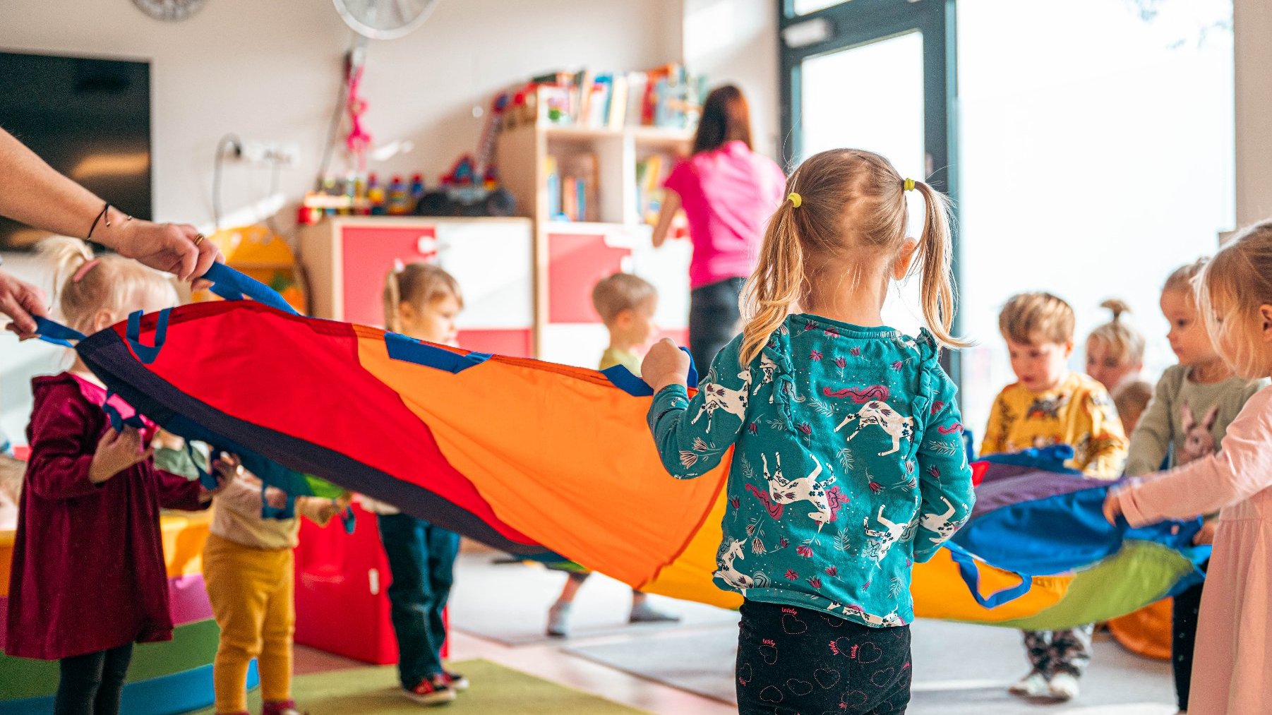 Zdjęcie przedstawia dzieci bawiące się chustą klanza w sali żłobkowej.