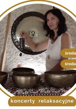 Kobieta w białej bluzce siedzi na dywanie. Przed nią stoją misy i gongi do grania.