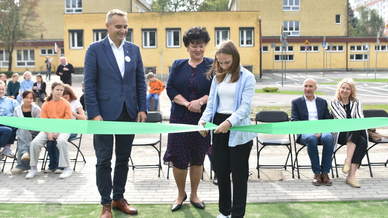 Zdjęcie przedstawia uczennicę przecinająca wstęgę. Obok stoi dyrektorka szkoły i wiceprezydent.