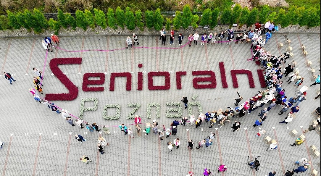 Na zdjęciu grupa ludzi wokół napisu z kwiatów: senioralni Poznań - grafika artykułu