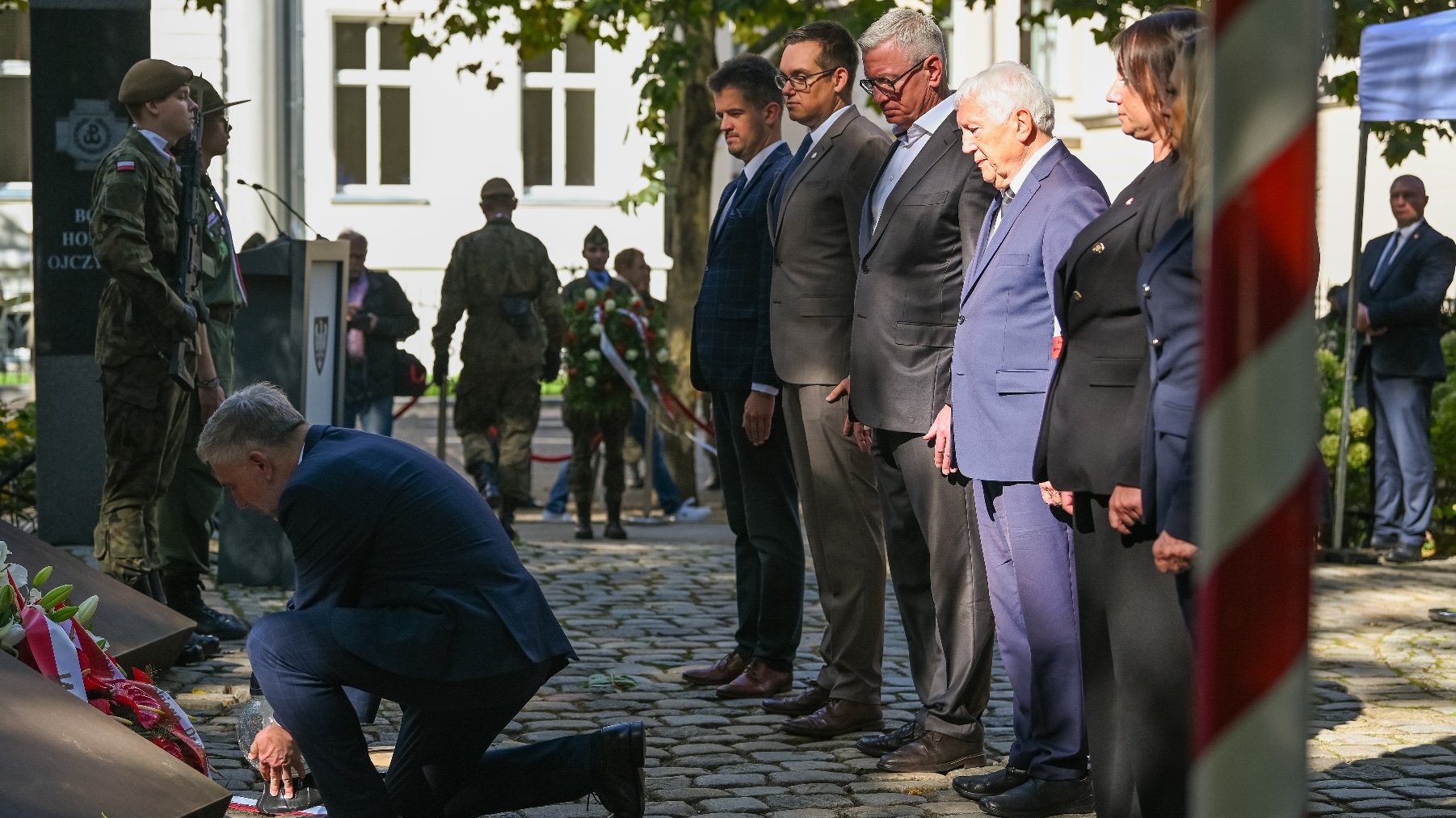 Zdjęcie przedstawia ludzi podczas składania kwiatów.