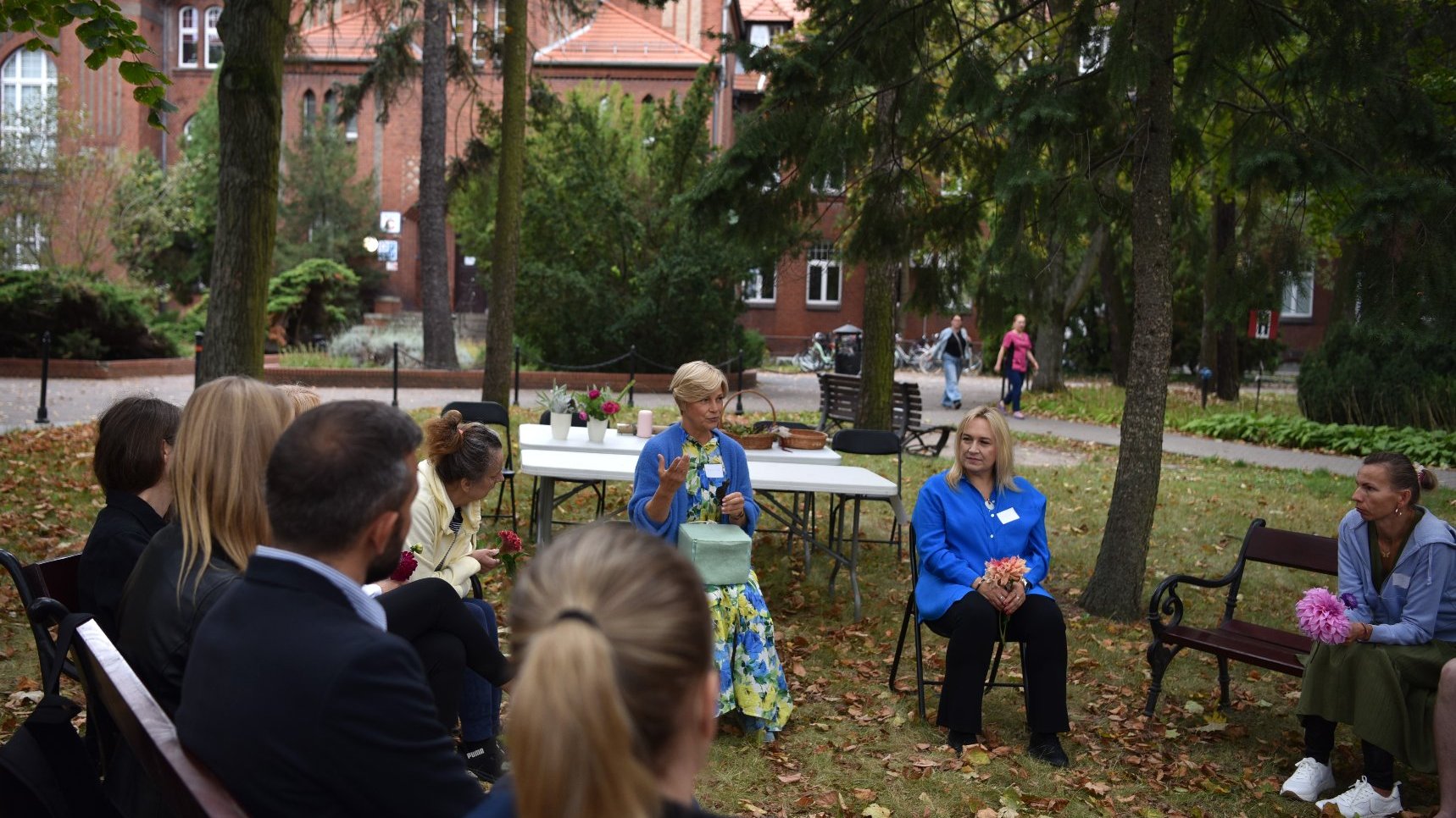 Zdjęcie przedstawia pacjentów i pracowników szpitala siedzących w kręgu podczas warsztatów w przyszpitalnym ogrodzie.