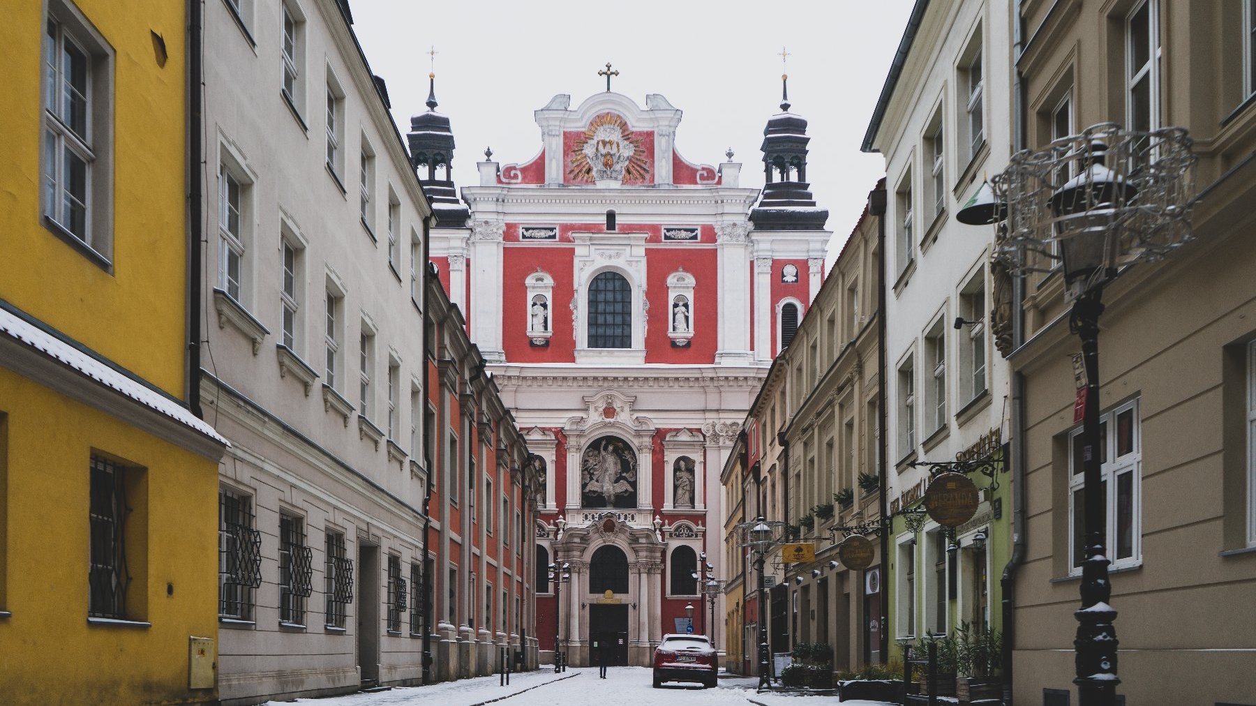 Na zdjęciu poznańska ulica, w tle fara, wszystko pokryte cieńką warstwą śniegu