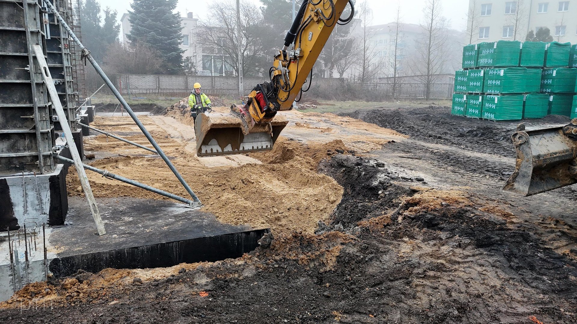 Na zdjęciu plac budowy, na pierwszym planie koparka, w tle robotnik