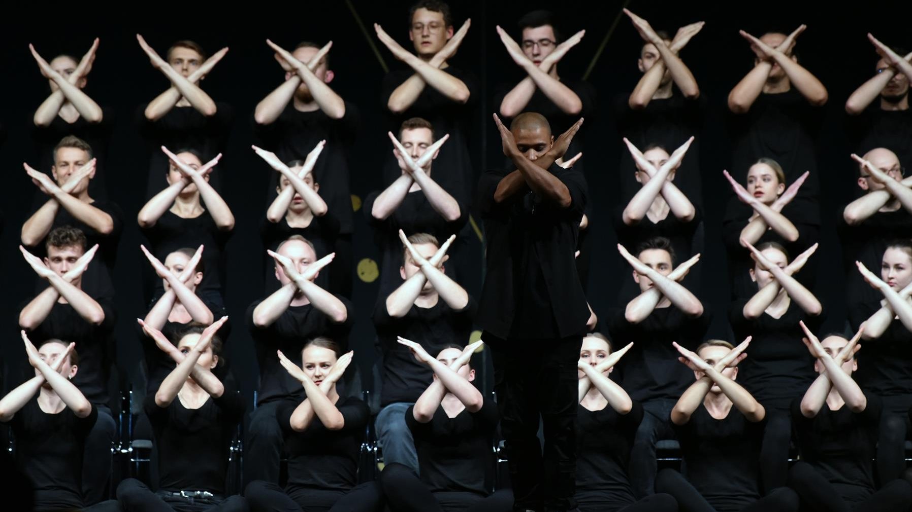 Na zdjęciu grupa tancerzy, wszyscy mają ręce złożone w znak X
