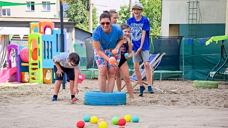 Uczestnicy zabaw podczas wrzucania piłeczek do ustawionej przed nimi opony.