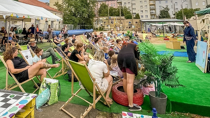 Publiczność siedząca na leżakach przed sceną na której występuje przebieraniec.