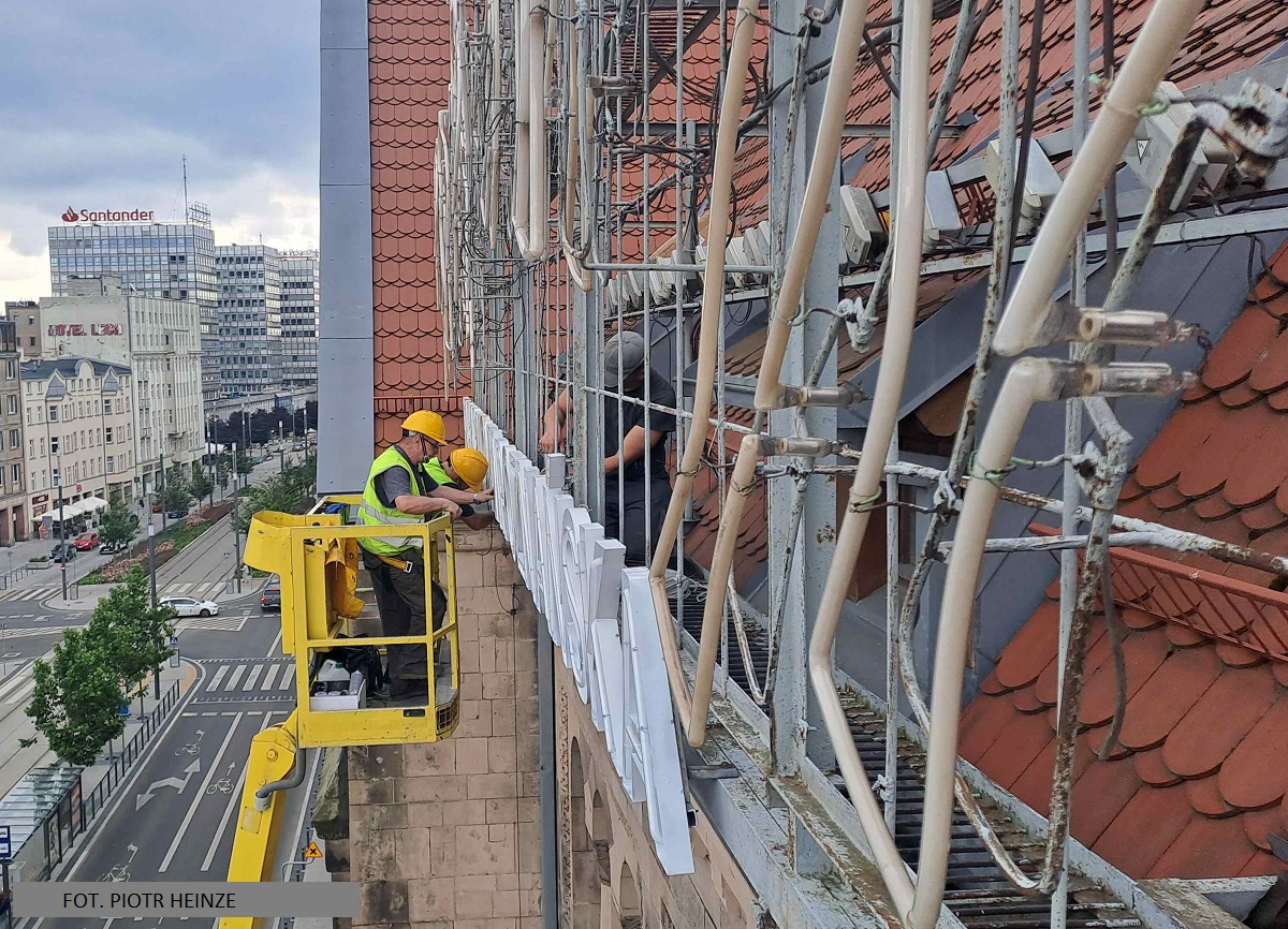 Fachowcy na rusztowaniu wykonujący prace przy rekonstrukcji neonu na budynku Filharmonii w Poznaniu. - grafika artykułu