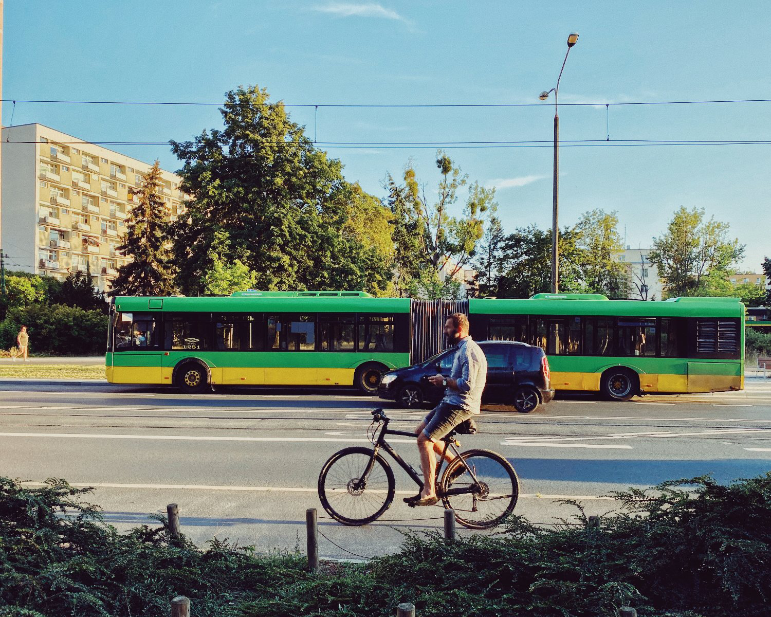 Mężczyzna jedzie na rowerze po ulicy bez trzymania kierownicy, w tle przejeżdża zielony autobus. - grafika artykułu